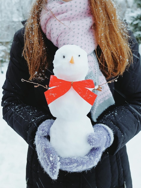 Sección media de una mujer sosteniendo a un muñeco de nieve en el patio