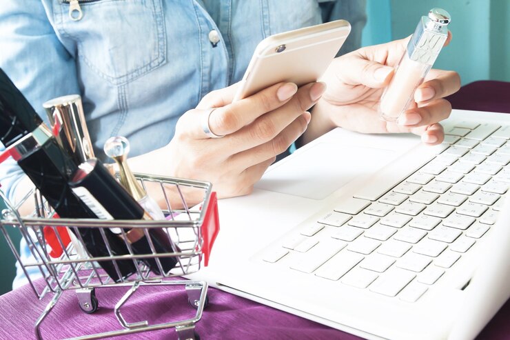 Foto sección media de una mujer sosteniendo un producto de belleza mientras usa un teléfono móvil con una computadora portátil en la mesa