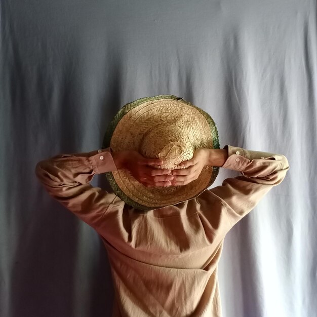 Sección media de una mujer sosteniendo un sombrero contra la pared
