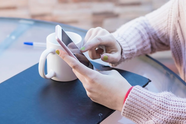 Foto sección media de una mujer sosteniendo un teléfono junto a una taza de café en la mesa