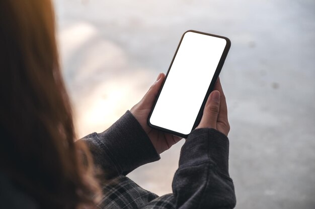 Sección media de una mujer sosteniendo un teléfono móvil en blanco mientras está sentada al aire libre