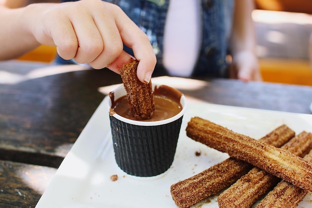 Foto sección media de una mujer sumergiendo churro en chocolate en la mesa