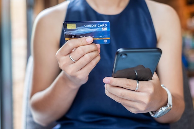 Sección media de una mujer con una tarjeta de crédito mientras usa el teléfono móvil para comprar en línea