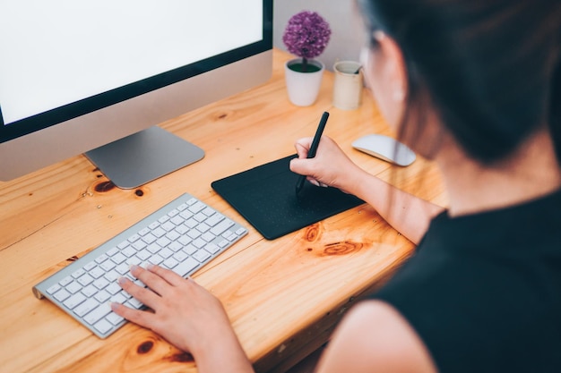 Sección media de una mujer usando una computadora y una tableta gráfica en el escritorio de la oficina