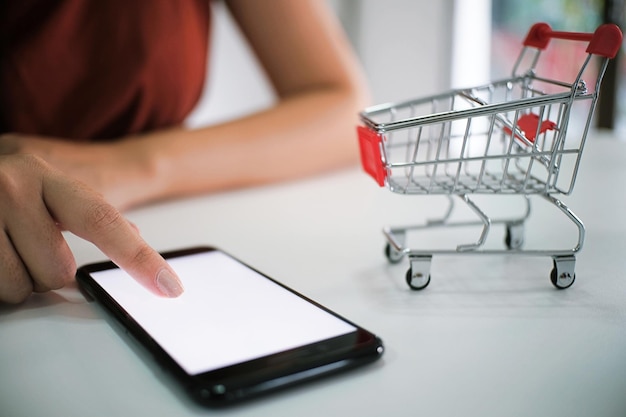 Sección media de una mujer usando un teléfono inteligente en el carrito de compras en la mesa
