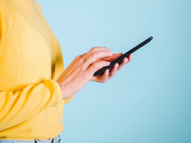 Sección media de una mujer usando el teléfono móvil contra la pared
