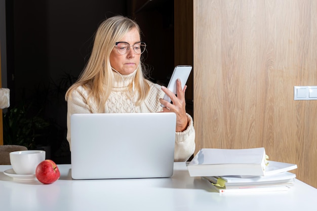 Sección media de una mujer usando un teléfono móvil mientras está sentada en la mesa