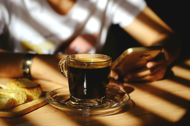 Sección media de una mujer usando un teléfono móvil con una taza de café en la mesa