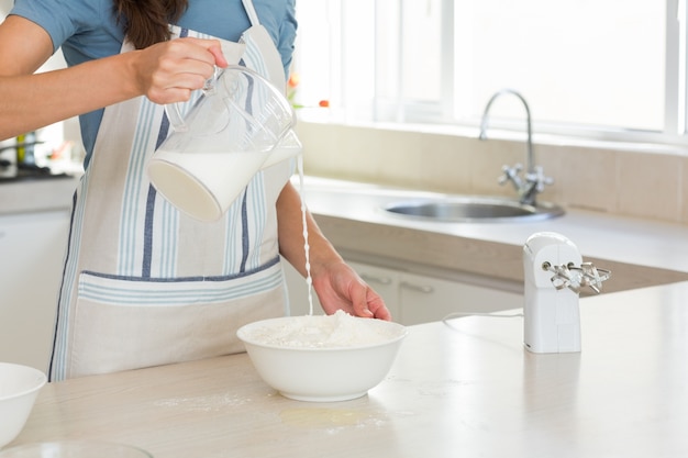 Sección media de mujer vertiendo leche en masa en la cocina