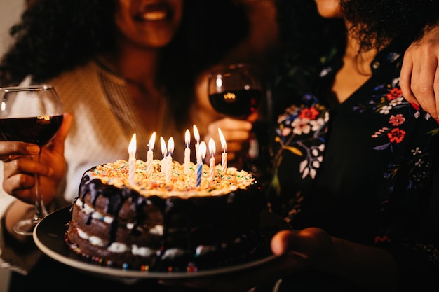 Sección media de mujeres con pastel de cumpleaños en el cuarto oscuro