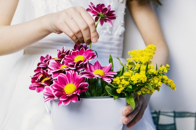 Sección media de una niña sosteniendo flores contra la pared