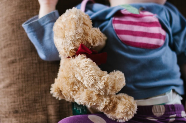 Foto sección media de un niño con un oso de peluche tendido en la cama en casa