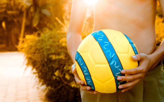 Foto sección media de una pelota de fútbol de hombre sin camisa mientras está de pie contra las plantas