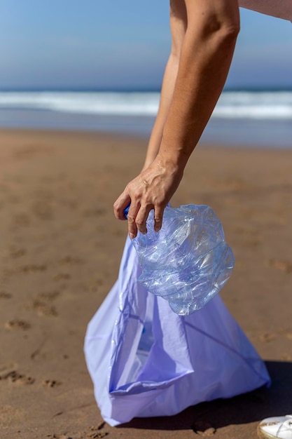 Foto sección media de una persona con una bolsa de plástico en la arena en la playa