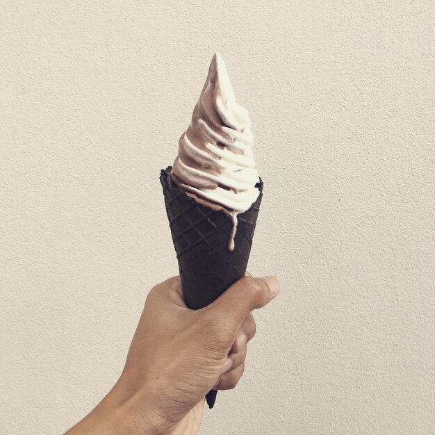 Sección media de una persona sosteniendo un helado contra la pared