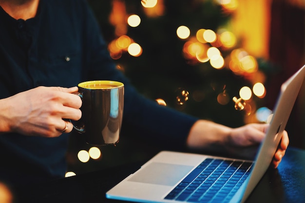 Sección media de una persona con una taza de café usando una computadora portátil