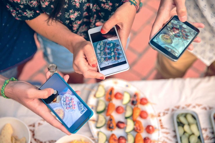 Foto sección media de personas fotografiando comida en la mesa con teléfonos móviles