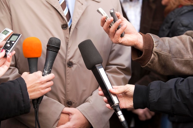 Sección media de un político dando una entrevista mientras los periodistas sostienen micrófonos