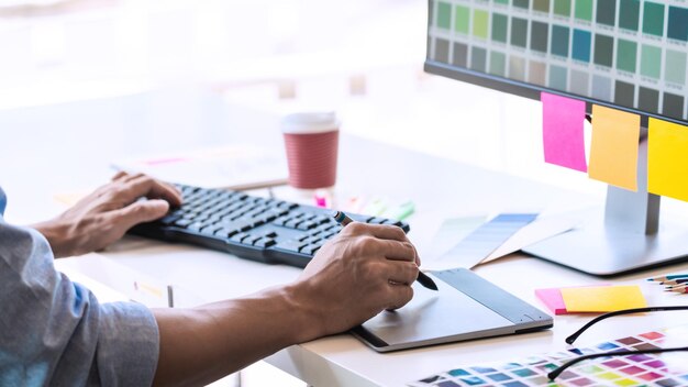 Sección media de un profesional del diseño que utiliza una tableta gráfica y una computadora en la mesa