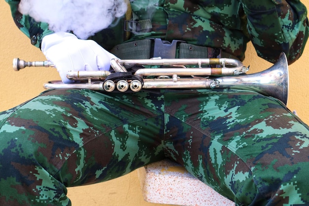 Sección media de un soldado del ejército con una trompeta sentada contra la pared