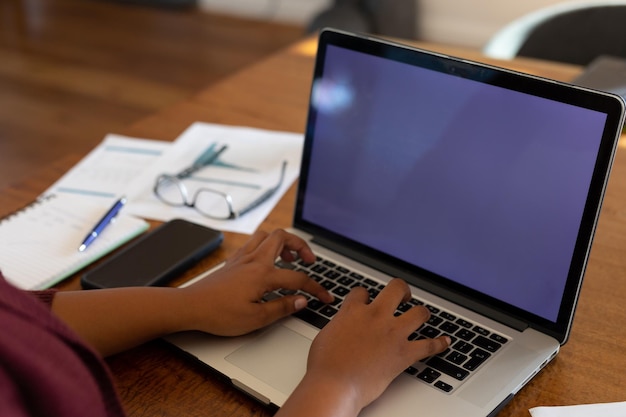 Sección media de tamaño grande mujer afroamericana sentada en la mesa, usando una computadora portátil con espacio para copiar