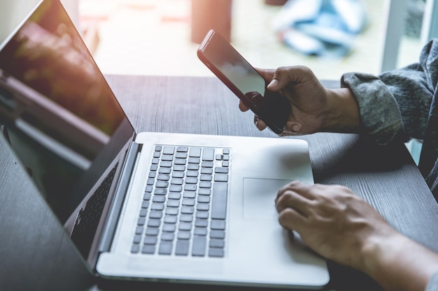 Sección media del teléfono móvil y la computadora portátil del hombre de negocios en la mesa