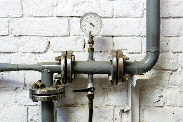 Sección de tubería del sistema de calefacción con manómetro, válvula y accesorios, contra una pared de ladrillos enlucidos