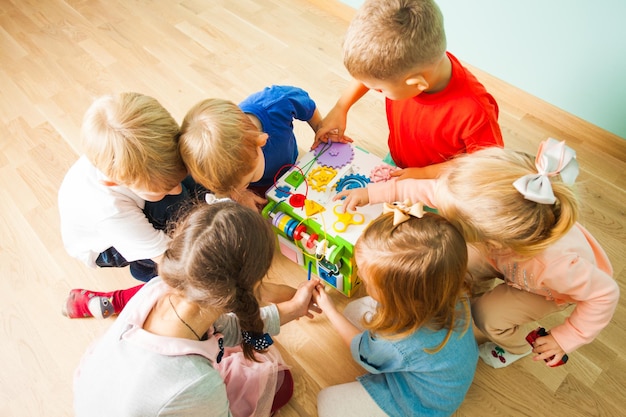 Sechs entzückende Kinder spielen mit neuem, farbenfrohem, ungewöhnlichem Spielzeug mit Sortierern, Schnürsenkeln und Reißverschlüssen. Fantasiespielzeug entwickeln. Ansicht von oben