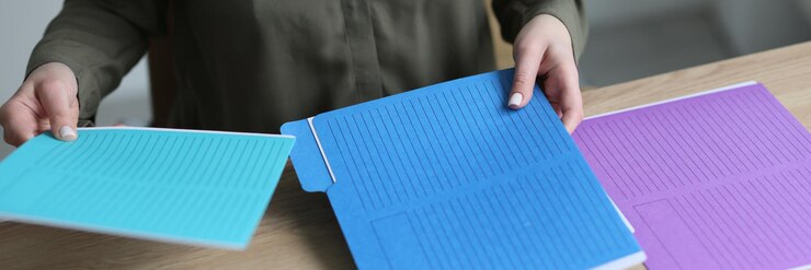 Foto secretaria ordena carpetas coloridas con materiales contables y documentos en mesa de madera