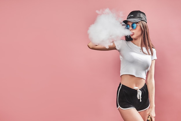 Seductora mujer joven de glamour de pie y vaping en rosa