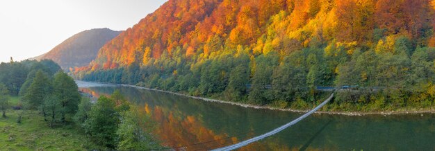 See hoch in den Bergen. Gelbe laubabwerfende und grüne Koniferen. Sonnenuntergang und blauer Himmel. Wunderbare Herbstlandschaft.