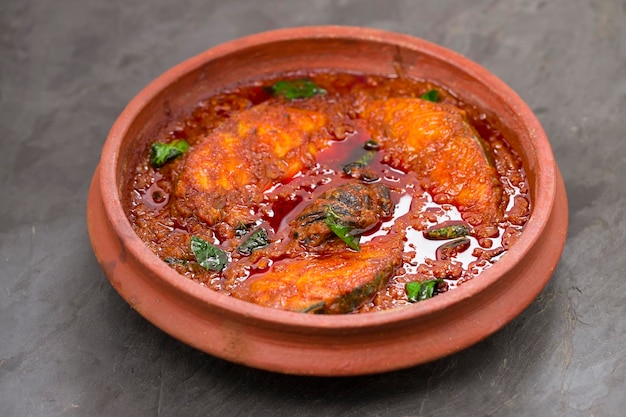 Foto seerfish oder kingfish curry traditionelles indisches fisch-curry im kerala-stil oder kottayam-stil, disharranged in einem steingut, garniert mit curryblättern und malabar-tamarinde auf grauem hintergrund