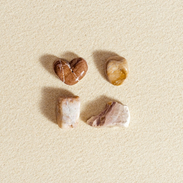 Seesteine Herzform auf natürlichem feinem Sandhintergrund Sommerquadratzusammensetzung aus Kieselsteinen
