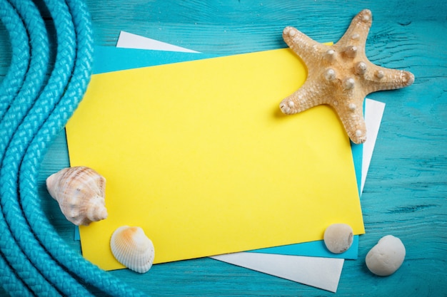 Seesterne, Kieselsteine und Muscheln liegen auf einer blauen Holzoberfläche mit Postkarte