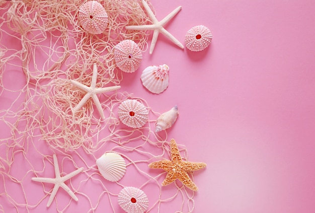 Seesterne, Seeigel, Fischernetz auf einem rosa Tisch