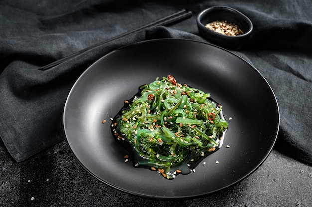 Seetang-Salat mit Sesam in einem Teller mit Stäbchen. Schwarzer Hintergrund. Draufsicht
