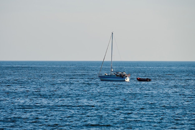 Segelboot, das auf blauem ruhigem Meer schwimmt, ruhiges Wetter, klarer Himmel. Schöner Meerblick mit Fischersegelboot und Motorboot. Segeln an sonnigen Tagen, Sommerabenteuerlandschaft. Landschaft am Meer