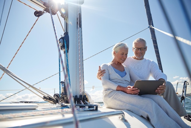 segeln, technologie, tourismus, reisen und personenkonzept - glückliches seniorenpaar mit tablet-pc-computer auf segelboot oder yachtdeck, das im meer schwimmt