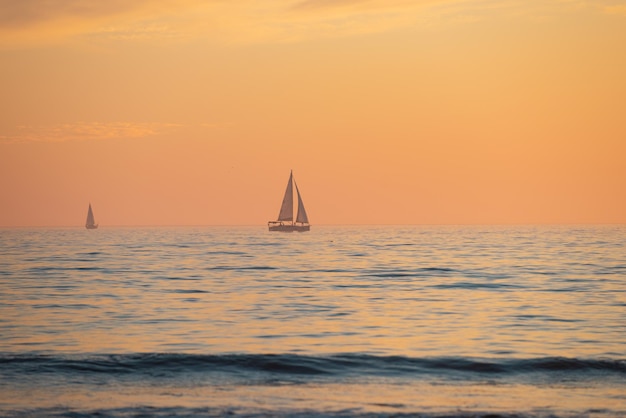 Segelyacht bei Sonnenaufgang. Ruhiges Meer mit Sonnenunterganghimmel und Sonne durch die Wolken vorbei. Ozean- und Himmelshintergrund, Meerblick.