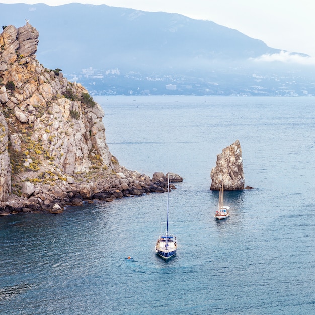 Segelyacht und Boot segeln entlang der felsigen Küste des Schwarzen Meeres zwischen Klippen und Bergen. Naturlandschaft und Seestück Krim, Russland.