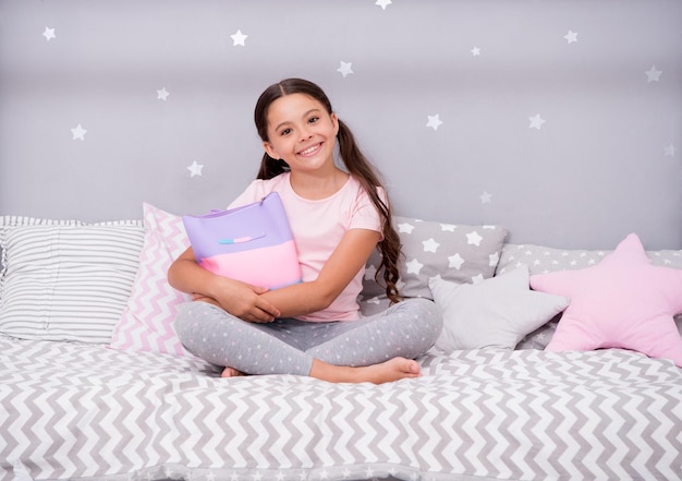 Segredos femininos Menina sente-se na cama com bolsa ou bolsa de cosméticos em seu quarto Garoto prepare-se para ir para a cama Tempo agradável no quarto aconchegante Garota garoto pijama fofo de cabelo comprido relaxando no quarto