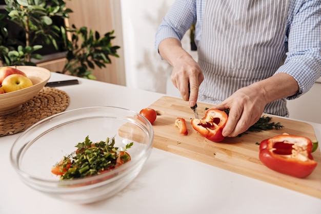 Seguindo a receita vegetariana. Hábil cozinheiro maduro e talentoso em pé na cozinha e cozinhando um prato vegetariano enquanto corta vegetais