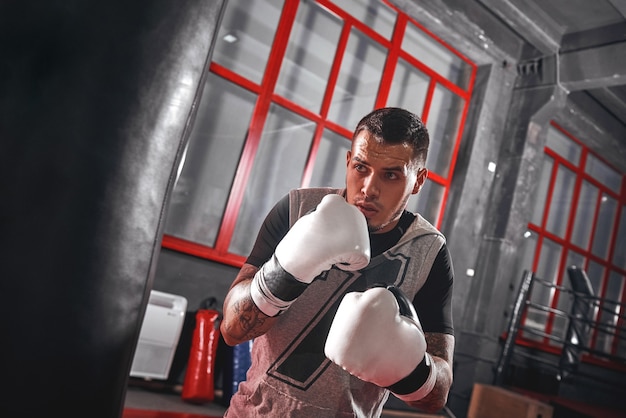 Foto un segundo antes del atleta tatuado enfocado en ropa deportiva boxeando en un saco de boxeo pesado mientras