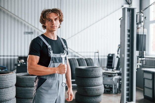 Segura a chave na mão Homem adulto de uniforme cinza trabalha no salão de automóveis