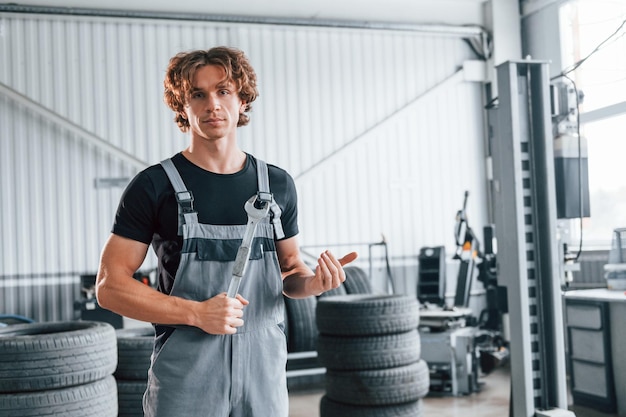 Segura a chave na mão homem adulto de uniforme cinza trabalha no salão de automóveis