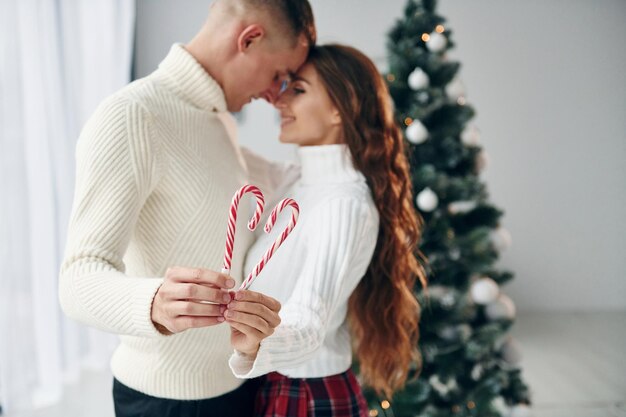 Segura doces nas mãos Jovem casal romântico celebra o ano novo juntos dentro de casa