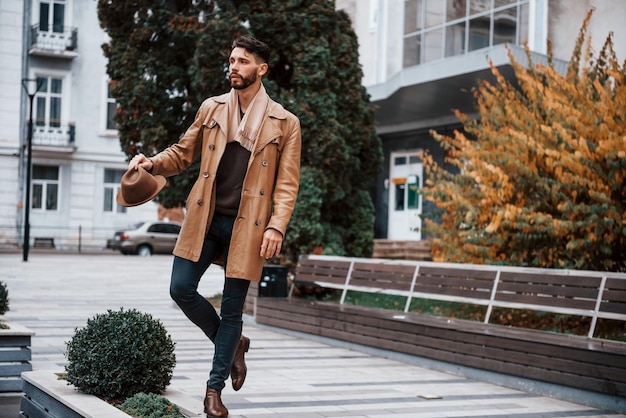 Segura o chapéu e posando Jovem modelo masculino em roupas da moda está ao ar livre na cidade durante o dia