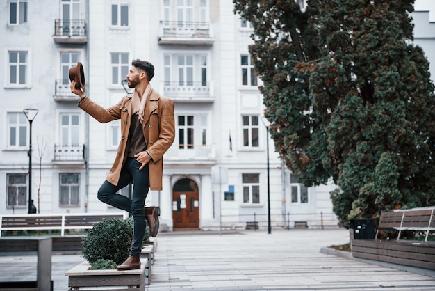 Segura o chapéu e posando Jovem modelo masculino em roupas da moda está ao ar livre na cidade durante o dia