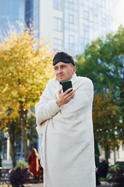 Segura smartphone Jovem de pijama está ao ar livre na rua Sente sono