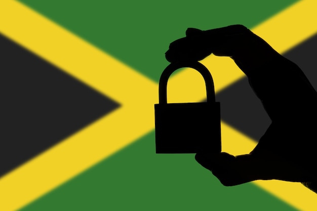 Segurança da Jamaica Silhueta de mão segurando um cadeado sobre a bandeira nacional